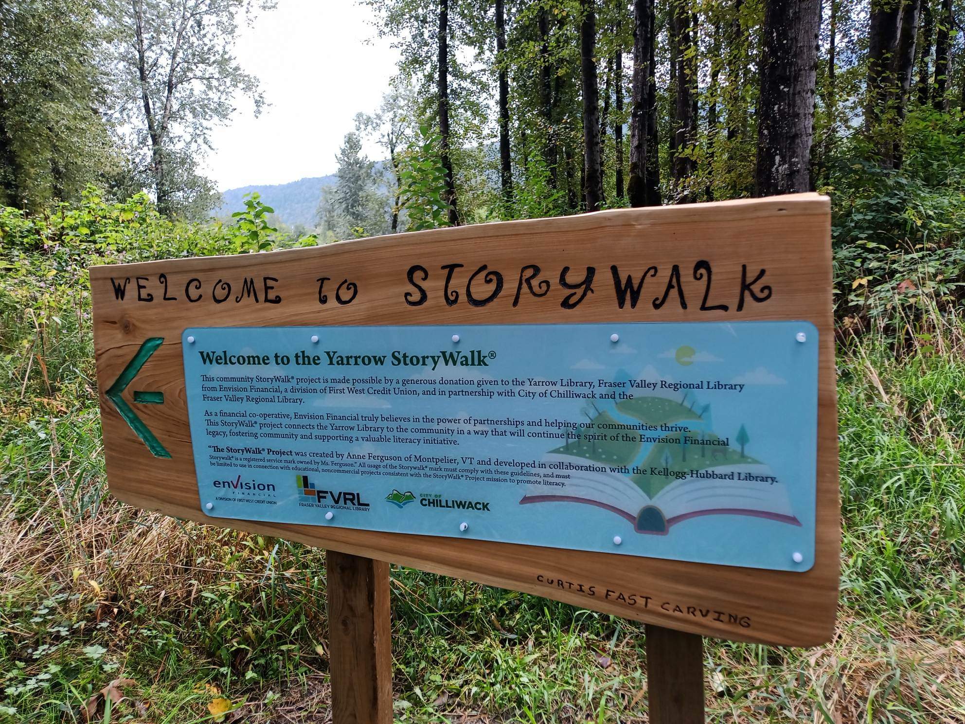 A wooden "Welcome to StoryWalk" sign with an arrow pointing left